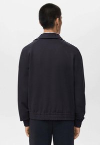 Navy blue jacket with a classic collar, ribbed cuffs, and elastic hem. Made from smooth fabric, showcasing a simple, clean design.