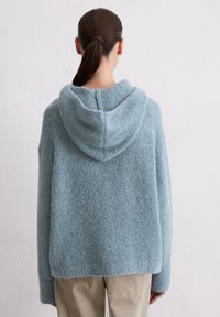 Przesadny hoodie z miękkiego, puszystego materiału w jasnoniebieskim kolorze. Posiada zaokrąglony kaptur oraz luźny krój z minimalną ilością szwów i detali.