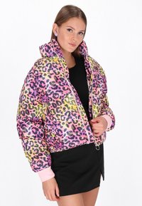 Színes leopárdmintás, párnázott dzseki fényes felülettel, rózsaszín mandzsettákkal, cipzáras záródással és bordázott aljjal. Fekete ruha alatta.