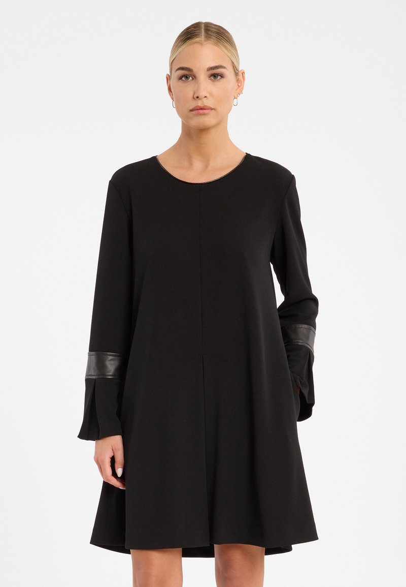 Schwarzes Kleid mit langen Ärmeln, das mit Lederakzenten an den Bündchen versehen ist. Hergestellt aus glattem Stoff, hat es einen runden Ausschnitt und eine ausgestellte Silhouette.