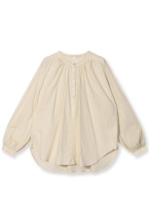 Bluzka z długim rękawem w jasnym beżowym kolorze, wykonana z miękkiego materiału, z okrągłym dekoltem, z przodem zapinanym na guziki oraz luźnym krojem i zaokrąglonym dołem.