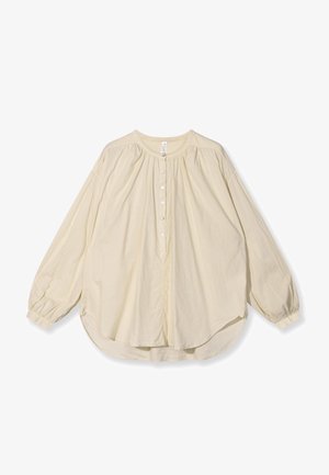 Bluzka z długim rękawem w jasnym beżowym kolorze, wykonana z miękkiego materiału, z okrągłym dekoltem, z przodem zapinanym na guziki oraz luźnym krojem i zaokrąglonym dołem.