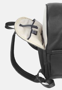 Svart läderryggsäck med dragkedja; insidan har beige foder och elastiska remmar för säker förvaring. Texturerad utsida och vadderade remmar.