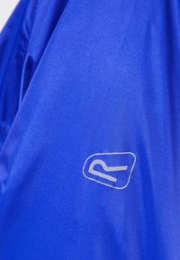 Tissu bleu avec un petit logo blanc en contour représentant une forme stylisée et abstraite rappelant la lettre R.