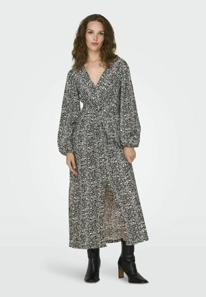 Pitkä, kietaisumallinen mekko musta-valkoisessa abstraktissa printissä, jossa on pitkät puffihihat ja sivuaukko. Yhdistetty mustiin nilkkureihin.