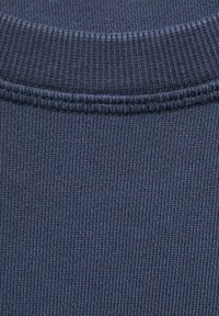 Tamno plavi rebrasti materijal dukserice s teksturiranim pletenjem. Ovratnik ima glatki, integrirani završetak s suptilnim detaljima šivanja.