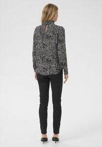 Schwarz-weiße Bluse mit Kragen, strukturiertem Muster, langen Ärmeln und einem Schlüsselanstich hinten, kombiniert mit enganliegenden schwarzen Hosen.