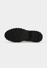 Semelle en caoutchouc noir d'une chaussure avec des crampons profonds et texturés, et le nom de la marque "Marc O'Polo" embossé près du centre.