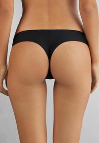 Svart bikiniunderdel med en mjuk, elastisk textur. Designad med en minimalistisk form och medelhög täckning bak. Ingen synlig hårdvara.