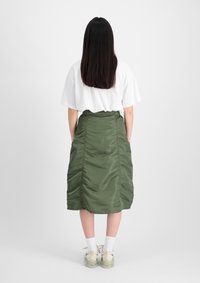 Gonna midi verde, arricciata, realizzata in un materiale lucido, abbinata a una maglietta bianca. Presenta un design semplice e una consistenza liscia.