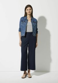 Jeansjack, witgestreepte top, marineblauwe wijde broek en zwarte sandalen met witte banden. Casual outfit met een relaxte pasvorm en eenvoudig ontwerp.