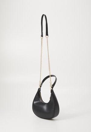 Sac à main en cuir noir en forme de croissant avec une bandoulière chaîne dorée et une fermeture éclair sur fond blanc uni.