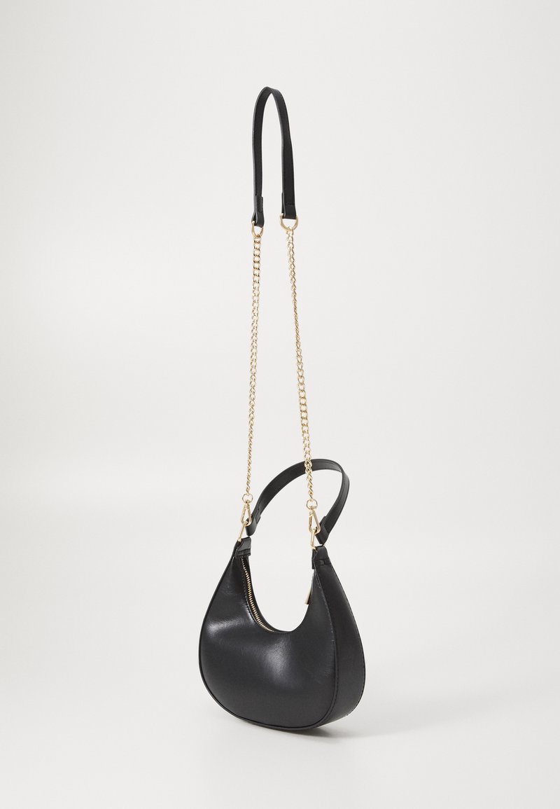 Sac à main en cuir noir en forme de croissant avec une bandoulière chaîne dorée et une fermeture éclair sur fond blanc uni.