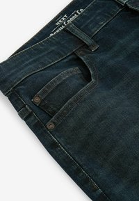 Vaqueros de mezclilla azul oscuro con un diseño clásico de cinco bolsillos, costuras visibles, un pequeño bolsillo delantero y una cinturilla con marca.