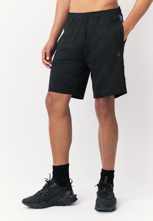 Pantaloni scurți atletici negri cu talie elastică, buzunare laterale și textură netedă. Asortați cu adidași negri ce au un design texturat.