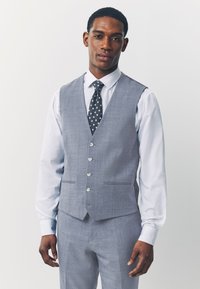 Gilet gris sur mesure à cinq boutons, associé à une chemise blanche et une cravate bleu marine à pois. Tissu lisse et coupe nette.