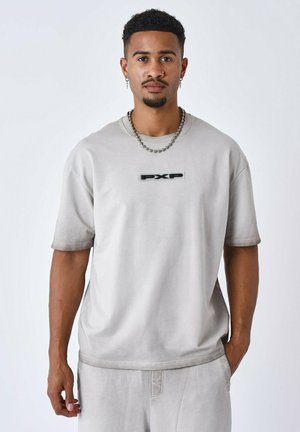 Camiseta de manga corta color gris claro, hecha de tela suave, con un logo negro "PXP" en el pecho y un corte relajado. Sin patrones distintivos.
