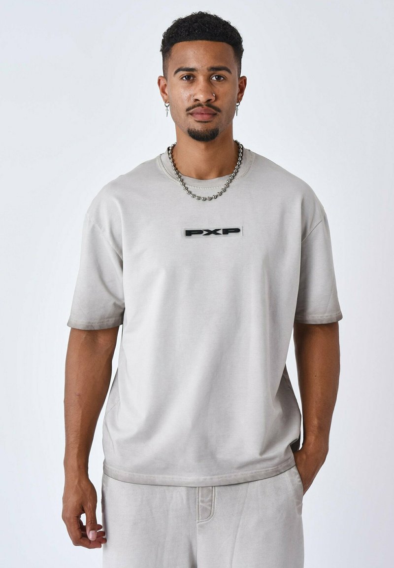 Camiseta de manga corta color gris claro, hecha de tela suave, con un logo negro "PXP" en el pecho y un corte relajado. Sin patrones distintivos.