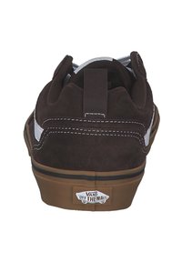 Zapatillas de skate de ante marrón con una franja lateral blanca, cuello acolchado y suela de goma color marrón. Presentan un parche con el logo en el talón.