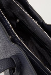 Sac à main structuré bleu marine avec un extérieur texturé, des détails de fermeture éclair en argent et une doublure en tissu présentant un motif rayé subtil.