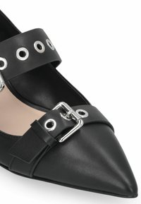 Chaussure en cuir noir à bout pointu avec deux larges brides ornées d'œillets argentés et d'une boucle métallique, mettant en valeur un design élégant.