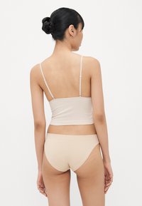 Beige katoenen top met dunne bandjes, aansluitend ontwerp en bijpassende naadloze bikini. Glad textuur met minimale stikdetails.