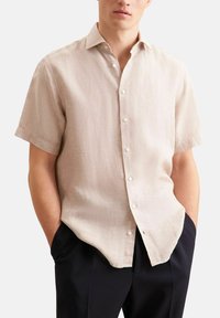 Korte mouwen beige linnen shirt met een knoopsluiting, voorzien van een subtiele textuur en een losse pasvorm. Draagt een zwarte broek.