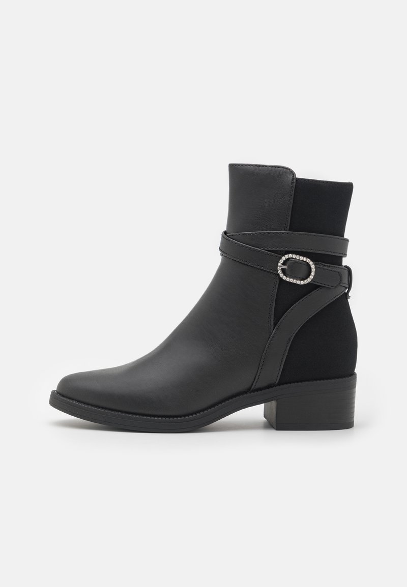 Bottine noire en cuir avec petit talon carré, sangle décorative et boucle ovale ornée de strass sur le côté.