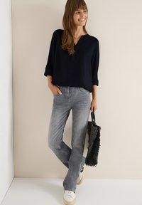 Marinebluse med V-udskæring og op-rullede ærmer, parret med grå lige ben jeans og en struktureret sort tote taske. Hvide sneakers fuldender looket.