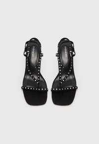 Sandale slingback negre din suede, cu un finisaj lucios, decorate cu accente cu cuie din argint și o curea subțire pentru glezne. Design cu toc plat.