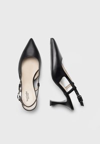 Tacchi slingback neri in pelle con punta affilata, che si assottigliano in una silhouette curva, dotati di un cinturino alla caviglia minimalista e di un tacco a spillo.