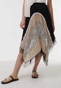 Plissé rok met een gelaagd ontwerp in zwart, beige en wit. Kanten details langs de zoom en tule accenten zorgen voor textuur.