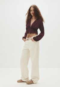 Burgundy, knyt-fram kort blus med långa ärmar; beige högmidjade vida jeans; ljusbruna sneakers med snördetaljer.