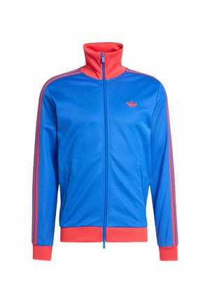 Giacca sportiva con zip blu con collo, polsini, fascia in vita e strisce sulle maniche di colore rosso, con piccolo logo Adidas rosso sul petto.