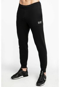 Pantaloni jogger neri a punta realizzati in tessuto morbido con vita elastica, dotati di un piccolo logo EA7 bianco sulla parte anteriore.