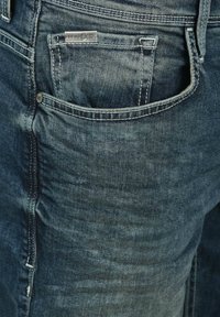 Jean en denim bleu foncé avec une texture délavée. Comprend une poche arrière et une étiquette métallique de marque portant l'inscription "Blend Since 1988".