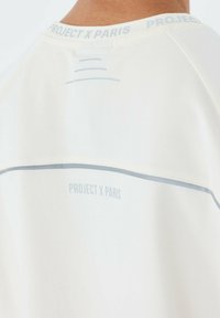 T-shirt atletico bianco con colletto rotondo, tessuto liscio, accenti grigi e testo stampato "PROJECT X PARIS" lungo la parte posteriore del collo.