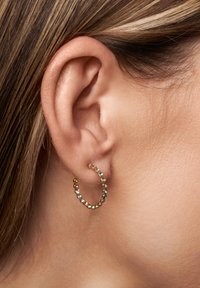 Pendientes de aro de oro adornados con pequeñas piedras azules y transparentes que brillan. El diseño presenta una forma circular con un acabado texturizado.