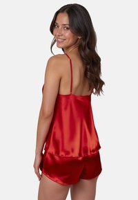 Rode satijnen camisole met dunne verstelbare bandjes en bijpassende shorts. Soepele textuur en een ontspannen pasvorm met een gelaagde zoomdetail.