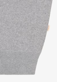 Pull gris en tricot avec ourlet et poignets côtelés, avec une petite étiquette de marque visible sur le côté. Texture douce et coutures régulières partout.