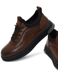 Chaussures en cuir marron avec des accents noirs, bout arrondi, semelle noire texturée et lacets à l'avant. Deux chaussures présentées sous un angle.