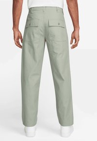 Light green cargo pants with a loose fit, featuring two back pockets with button closures and a smooth, textured fabric.