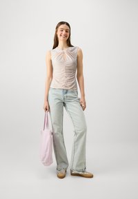Top sin mangas de color rosa claro con detalle de escote torcido y frunces laterales; combinado con vaqueros de pierna ancha de lavado claro y una bolsa de tote rosa.