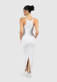 Vestido maxi gris ajustado con un diseño de espalda nadadora y una abertura lateral alta hasta el muslo, hecho de un tejido suave y elástico. Se lleva con zapatillas blancas.