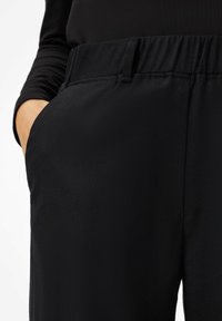 Pantalons noirs en tissu lisse avec une taille élastique, comportant une poche latérale et une coupe droite pour un ajustement décontracté.