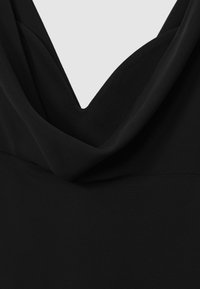 Černý bezrukávový top s volným výstřihem a hladkým, lehkým materiálem. Design zahrnuje hluboký tvar V na přední straně.