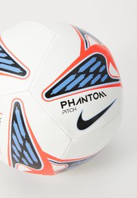 Nike Phantom futbola bumba baltā krāsā ar ziliem un sarkaniem akcentiem, kurai ir sešstūra raksts un izcili izdrukāts zīmola nosaukums.