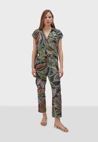 Salopette con fantasia floreale in tessuto scuro, con maniche corte, scollatura a V e vita con laccio. Presenta pantaloni a vestibilità ampia e sandali piatti.
