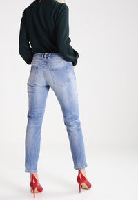 Ljust blå denimjeans med en smal passform, femfickdesign och subtila slitningar, som bärs tillsammans med glänsande röda högklackade skor och en mörkgrön topp.