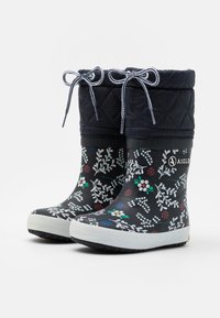 Bottes de cheville imperméables avec un motif floral noir, un haut matelassé, des semelles en caoutchouc blanches et des lacets ajustables bleu marine.